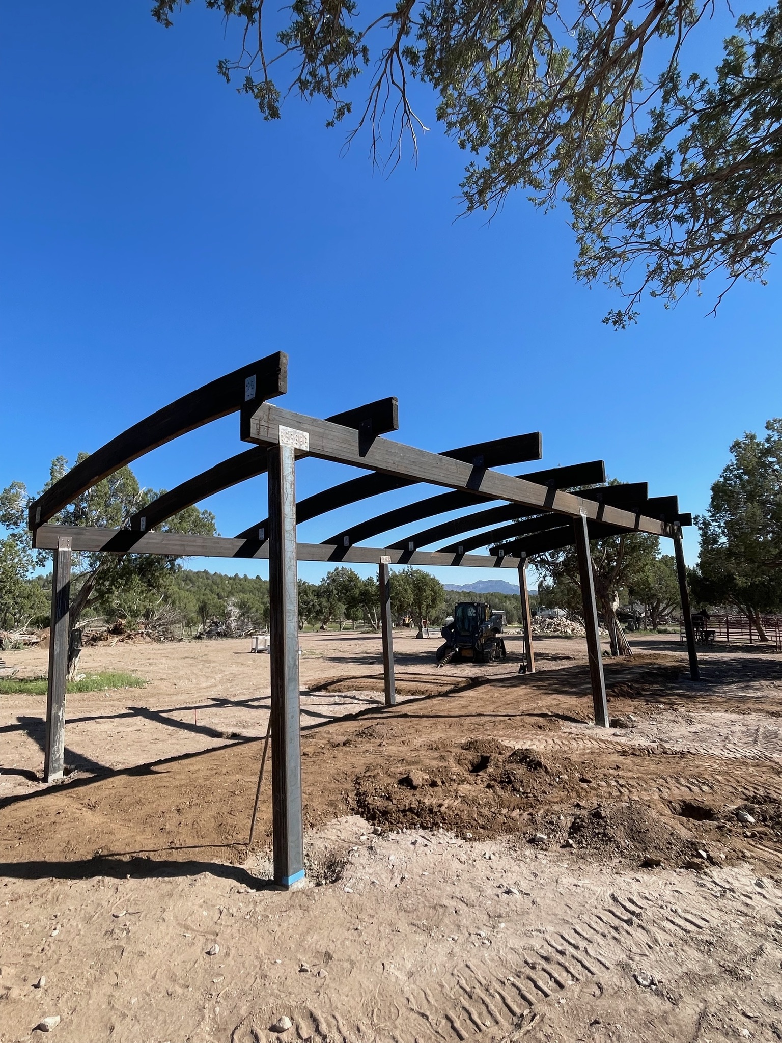 Steel and timber ramada shade structure with curved beams on a ranch property